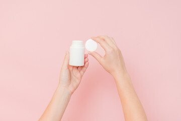 White bottle plastic tube in woman's hands on pink background. Packaging for pills, capsules or...