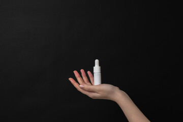 Hand holding serum glass bottle or essential oil with pipette on black background. Natural Organic...