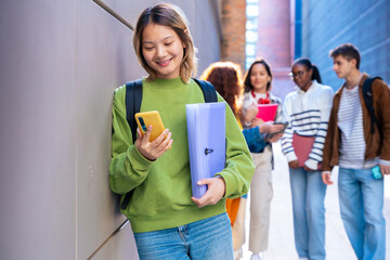 Happy young chinese woman browsing the internet using mobile device outdoors.