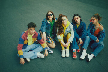 Group of friends wearing stylish 90s inspired outfits, posing on rooftop, having fun and joy. Urban style gathering. Concept of 90s, fashion, youth culture, old-style trends