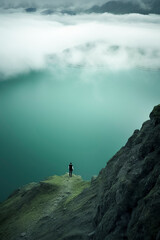 Obraz premium A solitary figure stands on a mountain edge, overlooking a vast, misty landscape, evoking awe and a sense of solitude