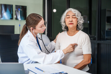 Caucasian woman checks an Asian elderly woman's heartbeat using a stethoscope. They communicate...