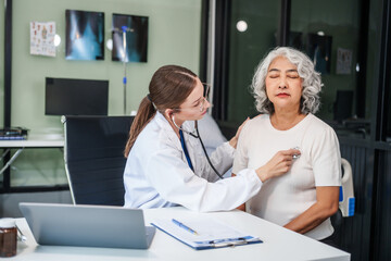 Caucasian woman checks an Asian elderly woman's heartbeat using a stethoscope. They communicate calmly and kindly.