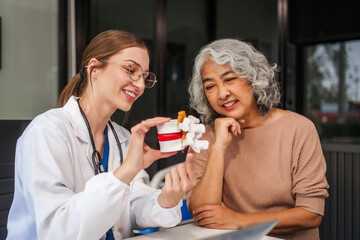  Caucasian woman assists an elderly Asian woman with a herniated disc, using a human anatomical lumbar disc herniation model for better understanding.