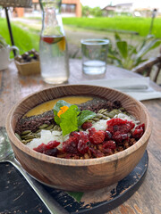 smoothie bowl of fruit in a wooden bowl on table, berries, nuts and mango sauce