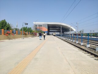 Fototapeta na wymiar Rails leading to an empty train station; 2 people in sight.