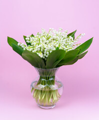 Bouquet lilies of the valley in a vase on a pink background. Congratulatory card. Selective focus.