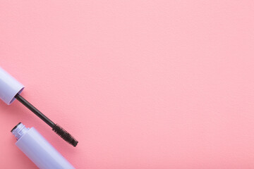Opened purple tube of black eyes mascara on light pink table background. Pastel color. Female beauty product. Closeup. Empty place for text. Top down view.
