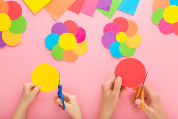 Young adult mother and child hands holding scissors, cutting paper and making colorful flower...