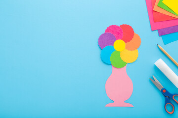 Colorful flower and vase shape, scissors, glue stick, pencil and application paper on blue table background. Pastel color. Closeup. Making decoration elements. Empty place for text. Top down view. - 801203193
