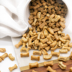 A close-up view of bone-shaped dog biscuits spilling out from a container onto a surface, ready for pets to enjoy.
