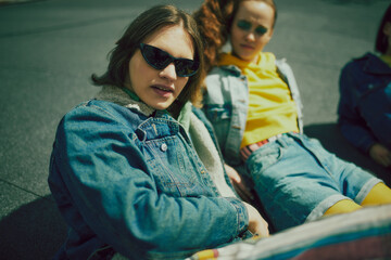 Stylish young man and woman wearing colorful clothes mixing with denim outfit, spending relaxing time on urban rooftop on sunny day. Concept of 90s, fashion, youth culture, old-style trends