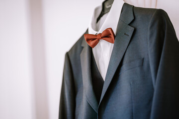 Valmiera, Latvia - August 19, 2023 - Close-up of a groom's dark blue suit with a white shirt and a copper bow tie, displayed against a clean white backdrop.