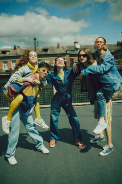 Joyful urban fashion vibe. Lively group of five friends enjoy sunny day on rooftop, wearing stylish denim clothes. Carefree, youthful spirit. Concept of 90s, fashion, youth culture, old-style trends