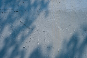 Close-up of a blue textured wall with subtle shadows of leaves, creating a serene and artistic...