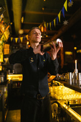 Experienced bartender shakes beverages with metal shaker. Barkeeper in black uniform productively...
