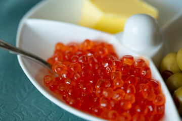 Red caviar in a white plate with olives, cheese and spoon
