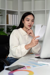 Asian woman freelance graphic designer working with color swatch samples and computer at desk in...
