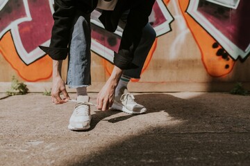 Person tying shoelaces, closeup shot, graffiti wall - Powered by Adobe