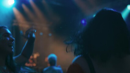 Two female friends wearing glitter holding drinks having fun dancing at outdoor summer music festival at night - shot in slow motion 