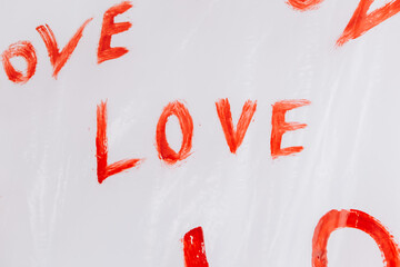 Multiple drawings of the word LOVE hand-painted in bright red forming a pattern on a plain white surface oilcloth, Valentine`s day concept celebration decoration in photo studio. Love, holiday, party