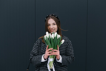 Young woman walking on the street with bouquet bunch of fresh spring tulips flowers, wind cold moody weather, celebrating International Women's Day. 8th of March holiday. Festive concept
