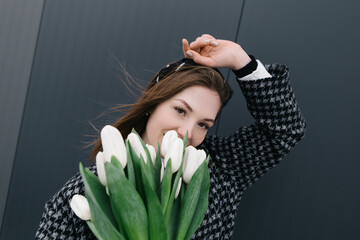 Young woman walking on the street with bouquet bunch of fresh spring tulips flowers, wind cold...