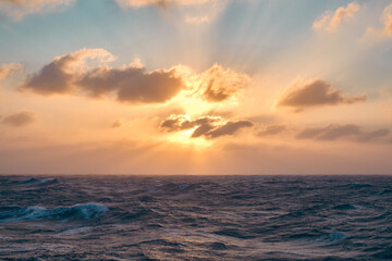 Sun shines through the clouds creating beams of light in the sky on the horizon.
