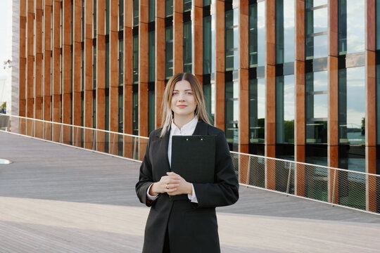 Businesswoman in a black suit with a folder in her hands in front of office building