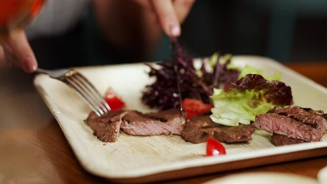 The girl cuts well-cooked, juicy meat on an ecological plate with a knife and fork. Delicious food without harm to the environment.