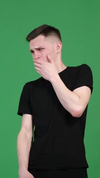 Unhappy and annoyed Caucasian man reacting to unpleasant, bad smell on green background. Yuck, displeased reaction. Vertical video.