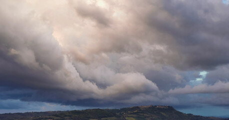 Enorme nuvola bianca sopra il paese in cima alla collina porta la pioggia in una giornata di sole invernale