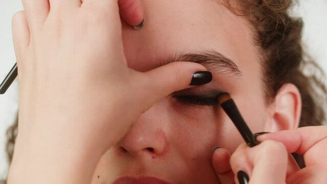 Eye shadow makeup to the upper eyelid, close-up. Makeup artist applies a bright eye shadow with a make-up brush.Tutorial master class of professional makeup, smoky eyes 