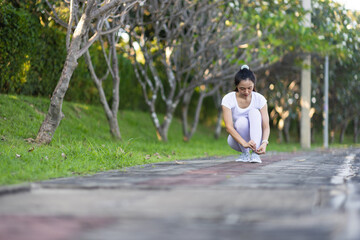 Young Asian woman jogging in the park tying her shoe laces and preparing to run.