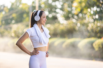 Beautiful Asian female runner wears headphones and listens to music while jogging.