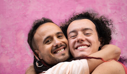 Close up headshot of two gay men lovers hug each other with smiles on their faces isolated on pink...