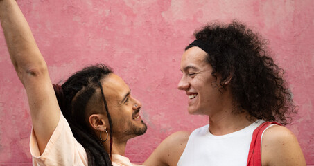 Two gay couple men are smiling and looking at each other with love and happiness isolated on pink background