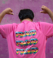 ear view of gay asian man wearing a pink shirt that says "Proud", embracing and supporting LGBTQ community
