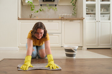 A woman washes the floor with her hands in a home kitchen, manual labor. Women's hands in yellow gloves while cleaning the kitchen