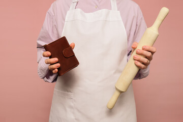 Woman cook with empty wallet on studio pink background. Portrait of a female person in chef's clothing