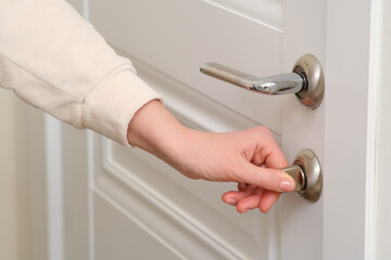 A woman's hand opens the lock of a white door, close-up