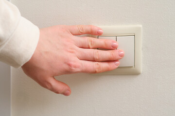 A woman's hand turns on the light with an electric switch, close-up