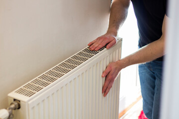 Man is checking radiator is it heating. Man warming his hands on the radiator. Home central heating system.