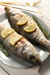 Delicious baked fish, lemon and rosemary on white wooden table