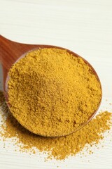 Curry powder in spoon on white wooden table, closeup