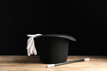Magician's hat, gloves and wand on wooden table against black background