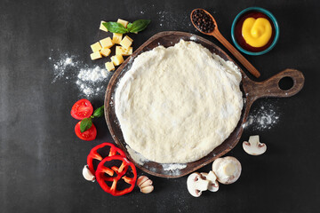 Pizza dough and products on dark table, flat lay