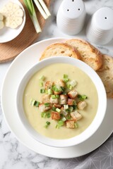 Tasty potato soup with croutons and green onion in bowl served on white marble table, flat lay