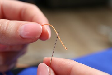 Woman inserting thread through eye of needle on blurred background, closeup