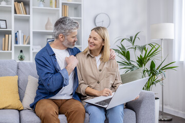 A cheerful mature couple enjoys some relaxed time together using a laptop in their elegantly furnished living room, exuding happiness and comfort.